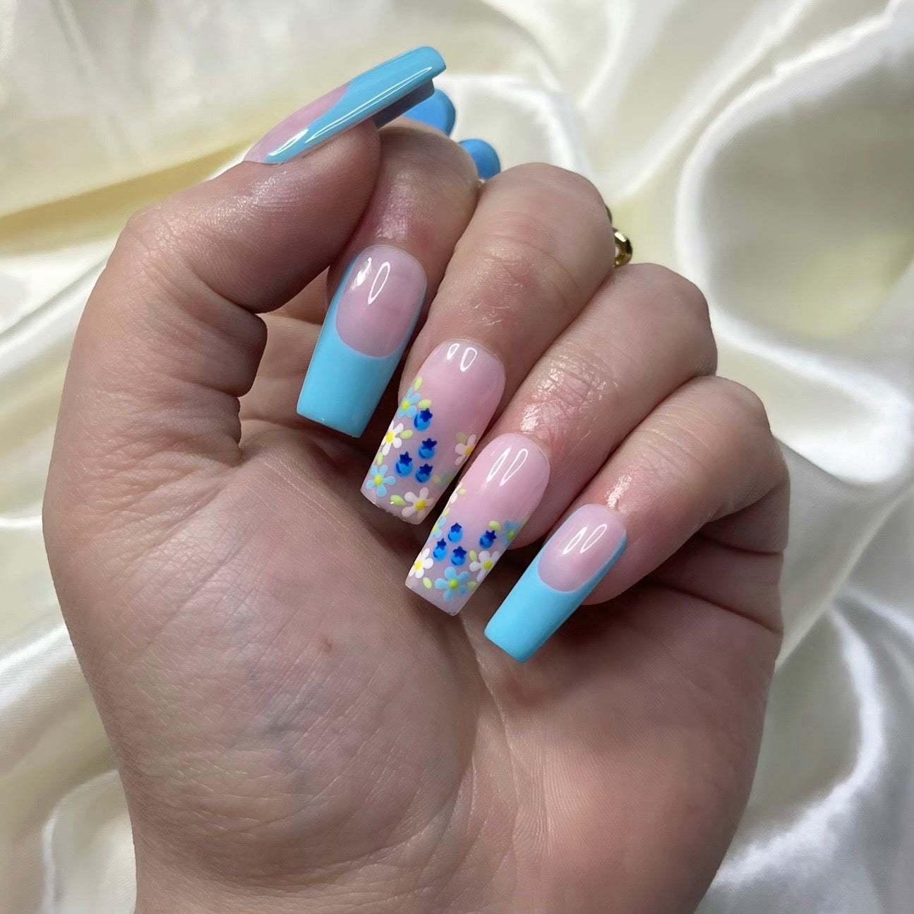 Blueberry Fields press-on nails feature blue French tips, floral designs, hand-painted blueberries, and soft pinky nude bases for a sweet, botanical spring look.